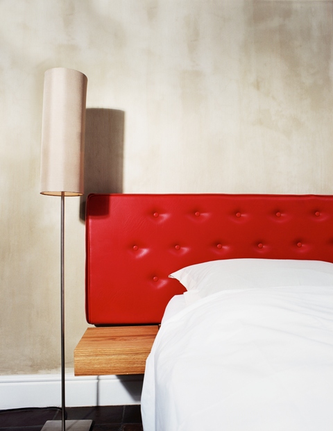 close-up of the side of a bed with a red leather headboard and a lamp beside it